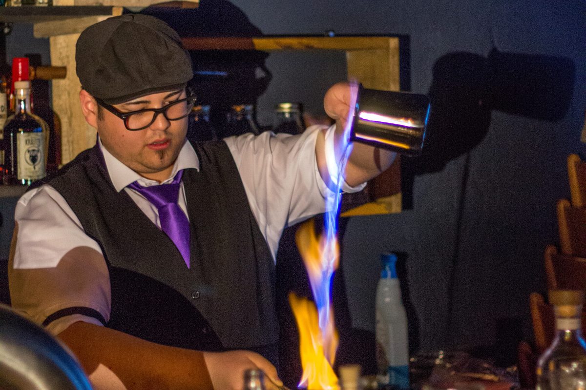 A bartender preparing a flaming blue blazer cocktail