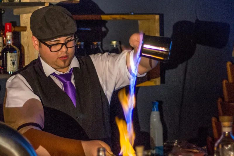 A bartender preparing a flaming blue blazer cocktail